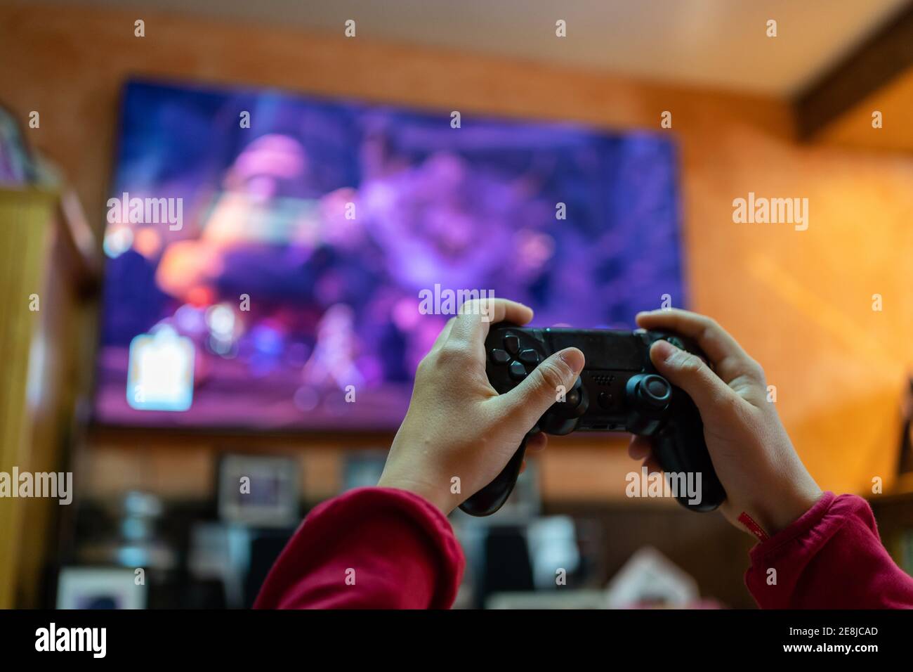 Crop persona anonima con controller che gioca video giochi in camera Con un grande schermo TV mentre si divertirà durante il fine settimana a casa Foto Stock