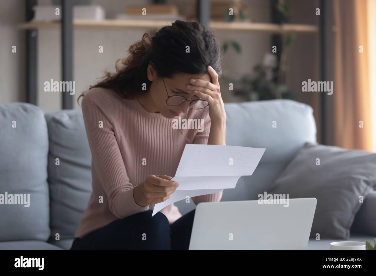 Stressato giovane donna caucasica leggere carta con cattive notizie. Foto Stock