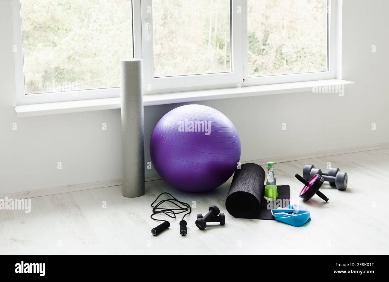 Camera vuota e luminosa, moderna e bianca, con accessori per l'allenamento a casa. Palla di yoga, banda in lattice per esercizi di resistenza, rullo in schiuma, pesi, corda di salto. Foto Stock