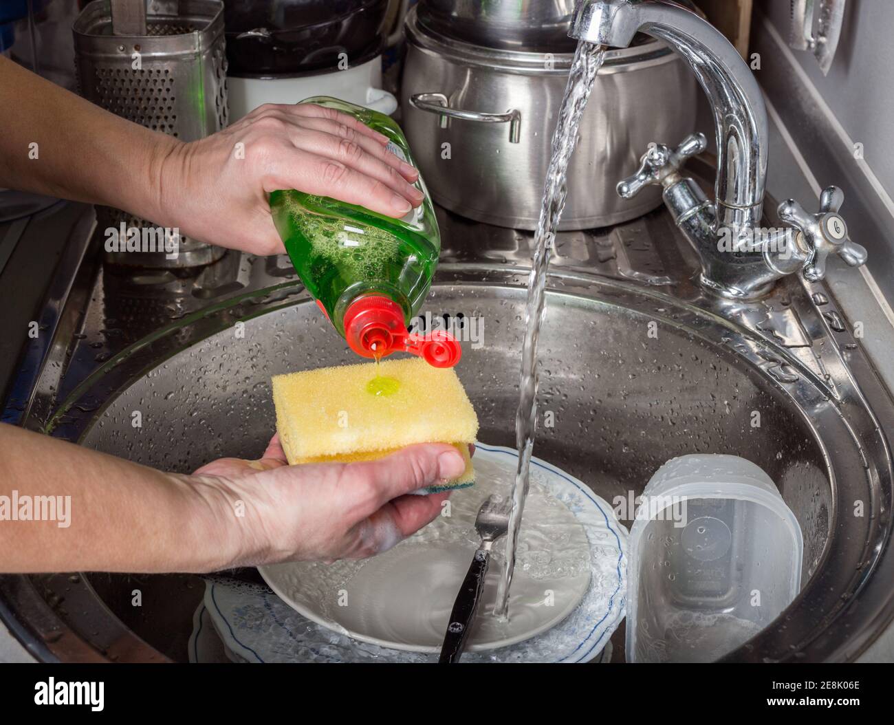 Compiti a casa - piatti di lavaggio. La donna anziana versa il liquido per il lavaggio dei piatti su una spugna Foto Stock