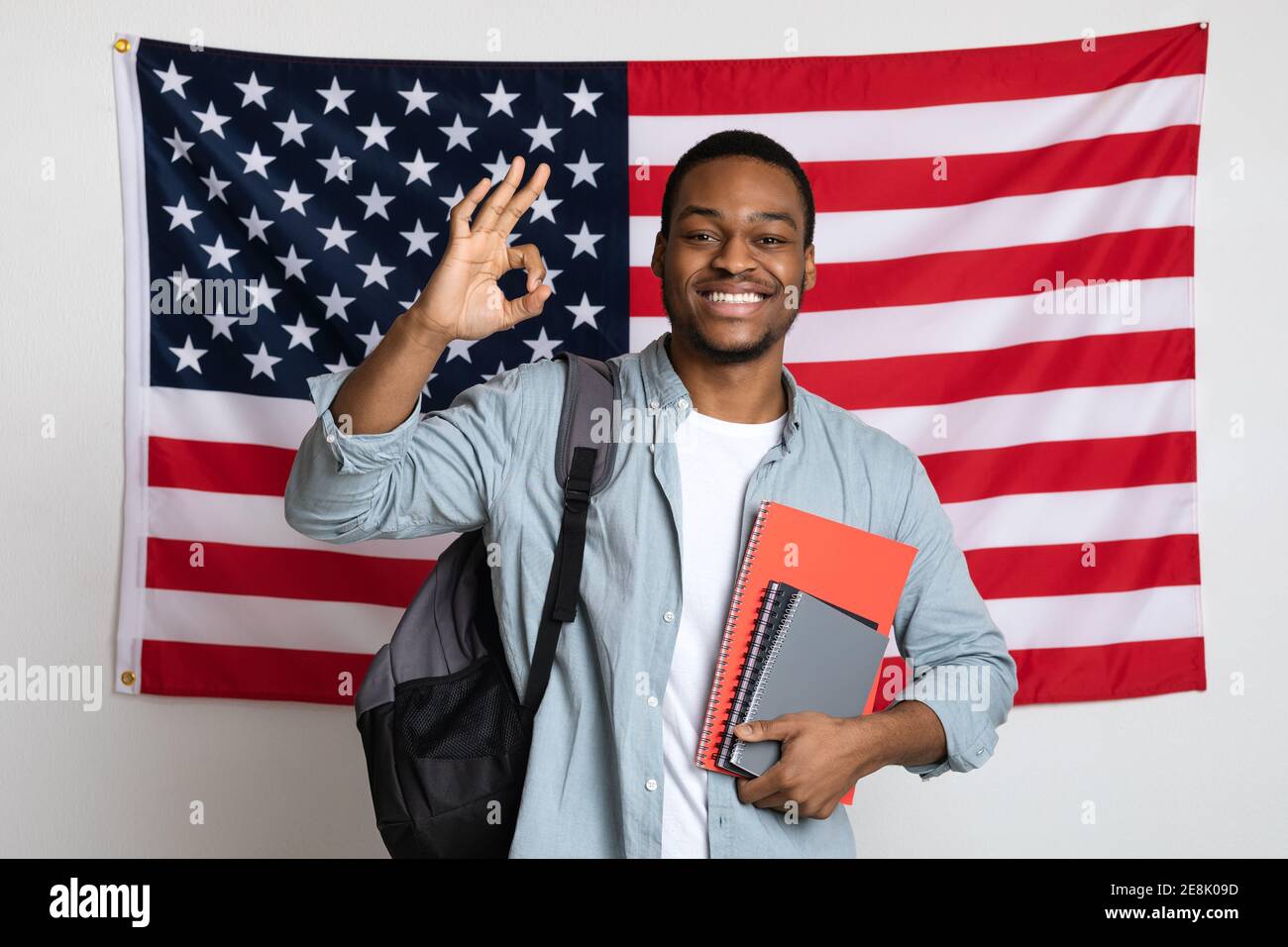 Sorridente studente di uomo nero in piedi sopra la bandiera americana, mostrando OK Foto Stock