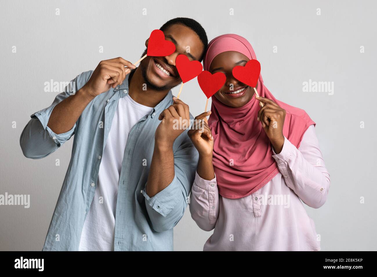 Giovane coppia musulmana nera che tiene i cuori rossi d'amore sopra gli occhi Foto Stock