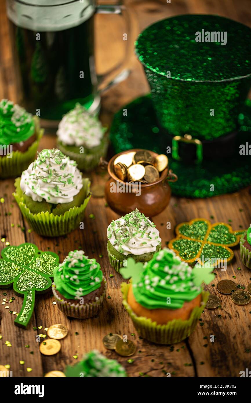 Concetto di giorno di San Patrizio con pentola d'oro, shamrock e cupcakes su sfondo di legno. Foto Stock