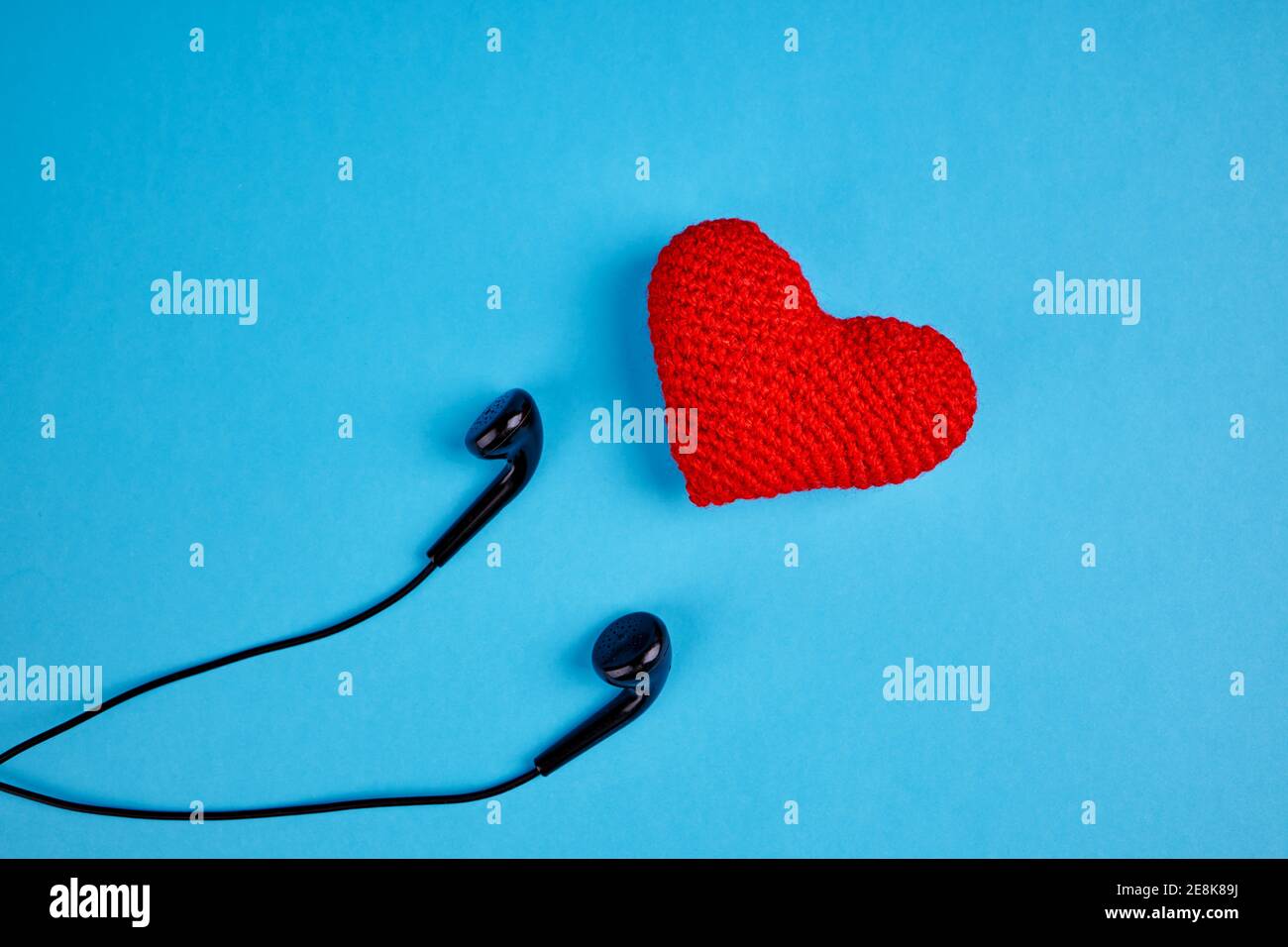 auricolari neri vicino al cuore rosso su sfondo blu con spazio per la copia. concetto di ritmo per l'amore per la musica Foto Stock