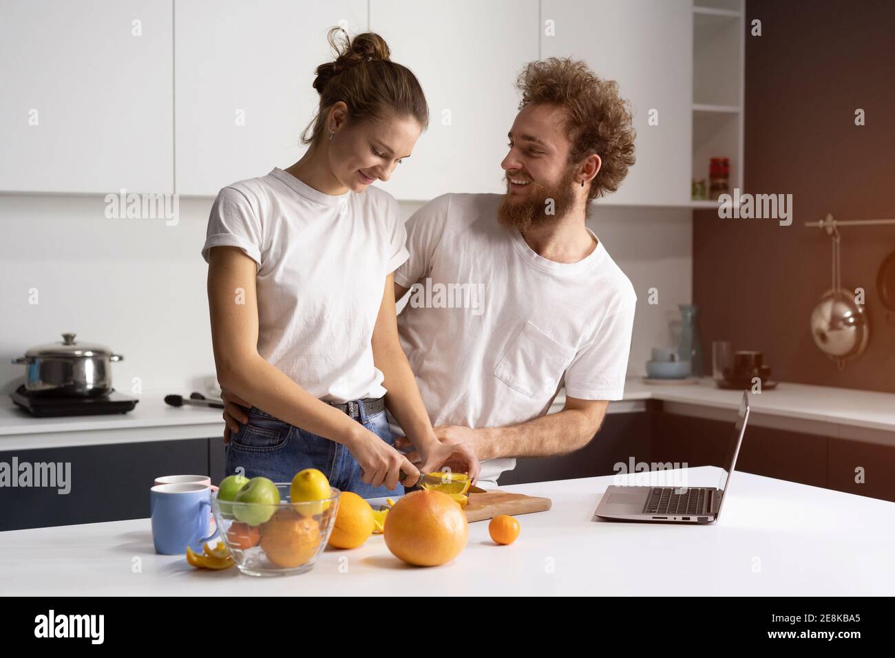 Felice della loro nuova giovane coppia di casa che cucinano cibo sano in nuova cucina guardando video in streaming online sul laptop. Bella giovane coppia che parla Foto Stock