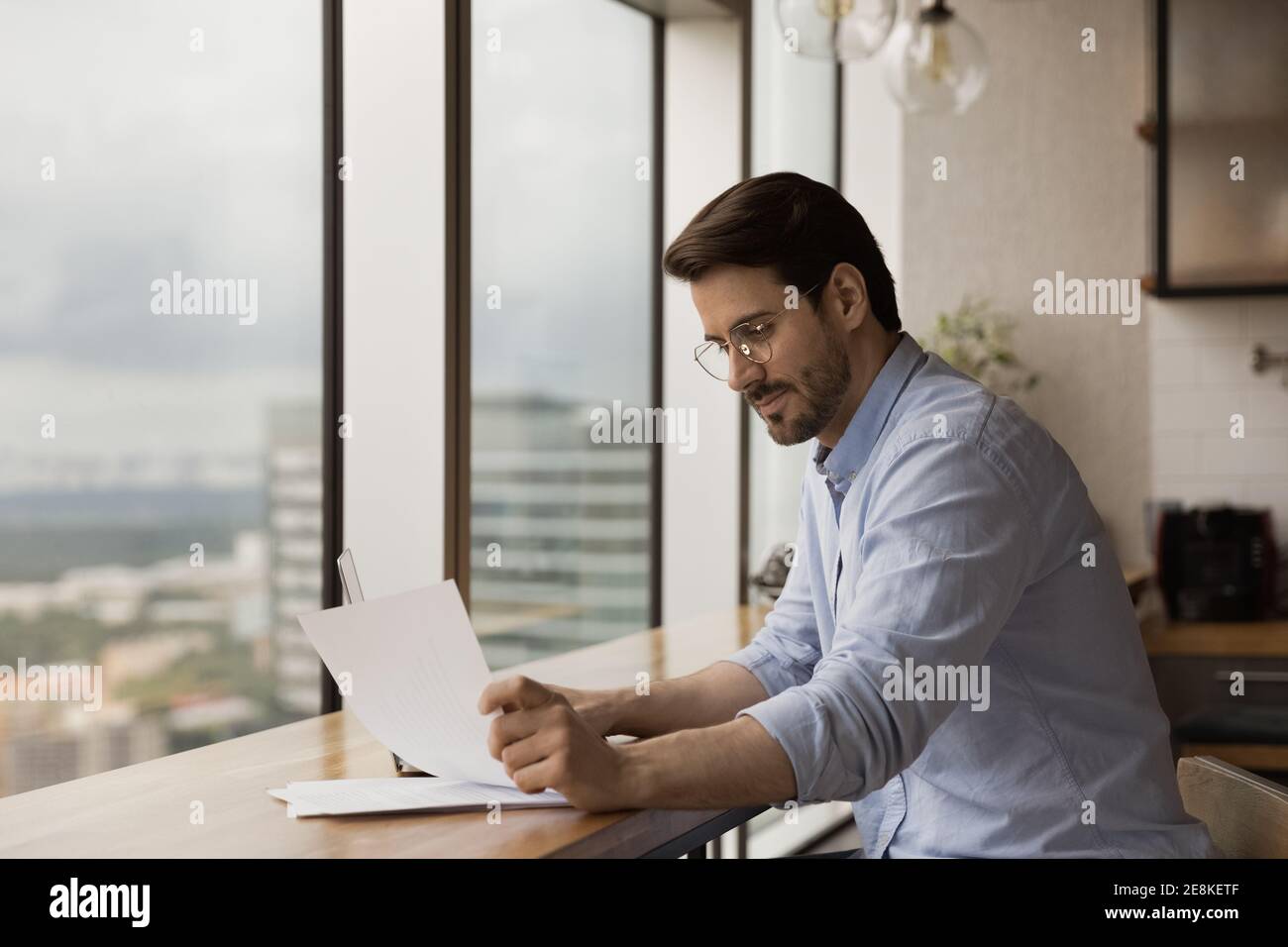 Un uomo d'affari che ha avuto successo a leggere il documento al banco di lavoro vicino alla finestra panoramica Foto Stock