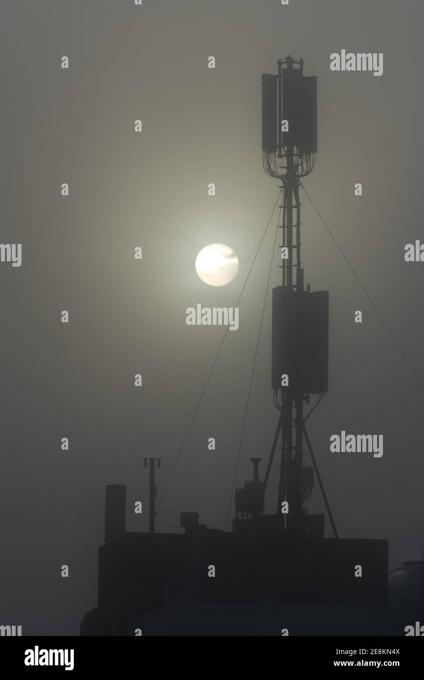 Torre di comunicazione su un edificio con antenna 4G 5G all'alba in nebbia. Foto Stock