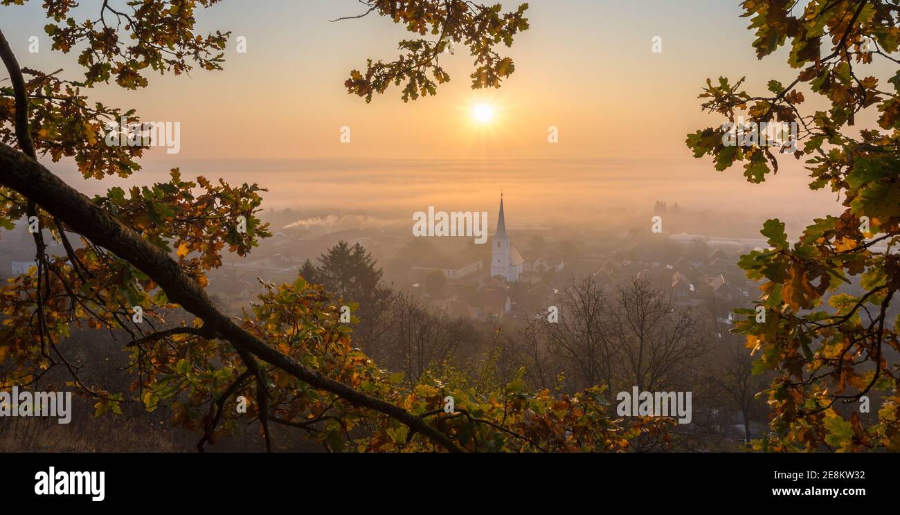 Vista panoramica panoramica di un'alba su un villaggio in una valle nebbiosa Foto Stock