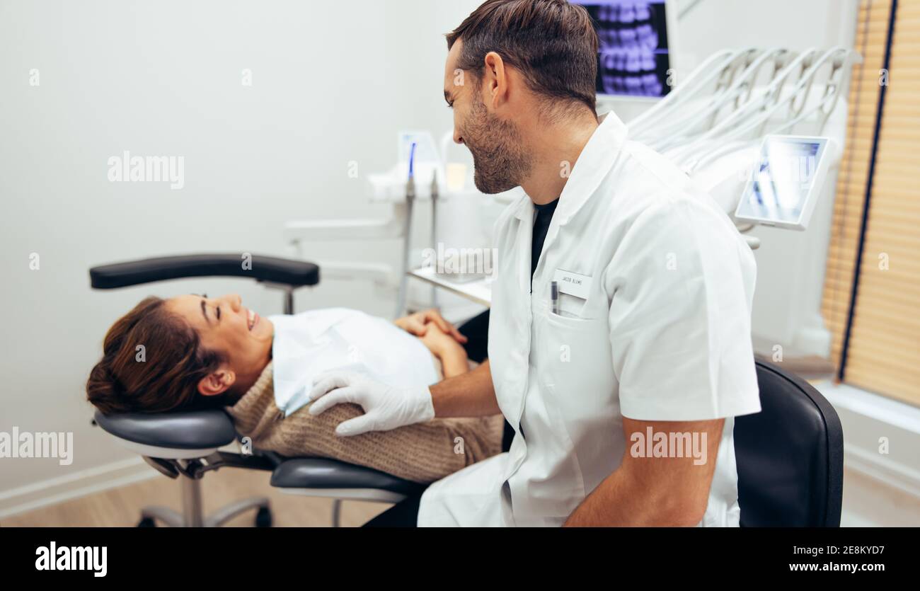 Dentista che parla con una paziente di sesso femminile seduto in sedia prima del trattamento. Paziente femminile e dentista sorridente in odontoiatria. Foto Stock