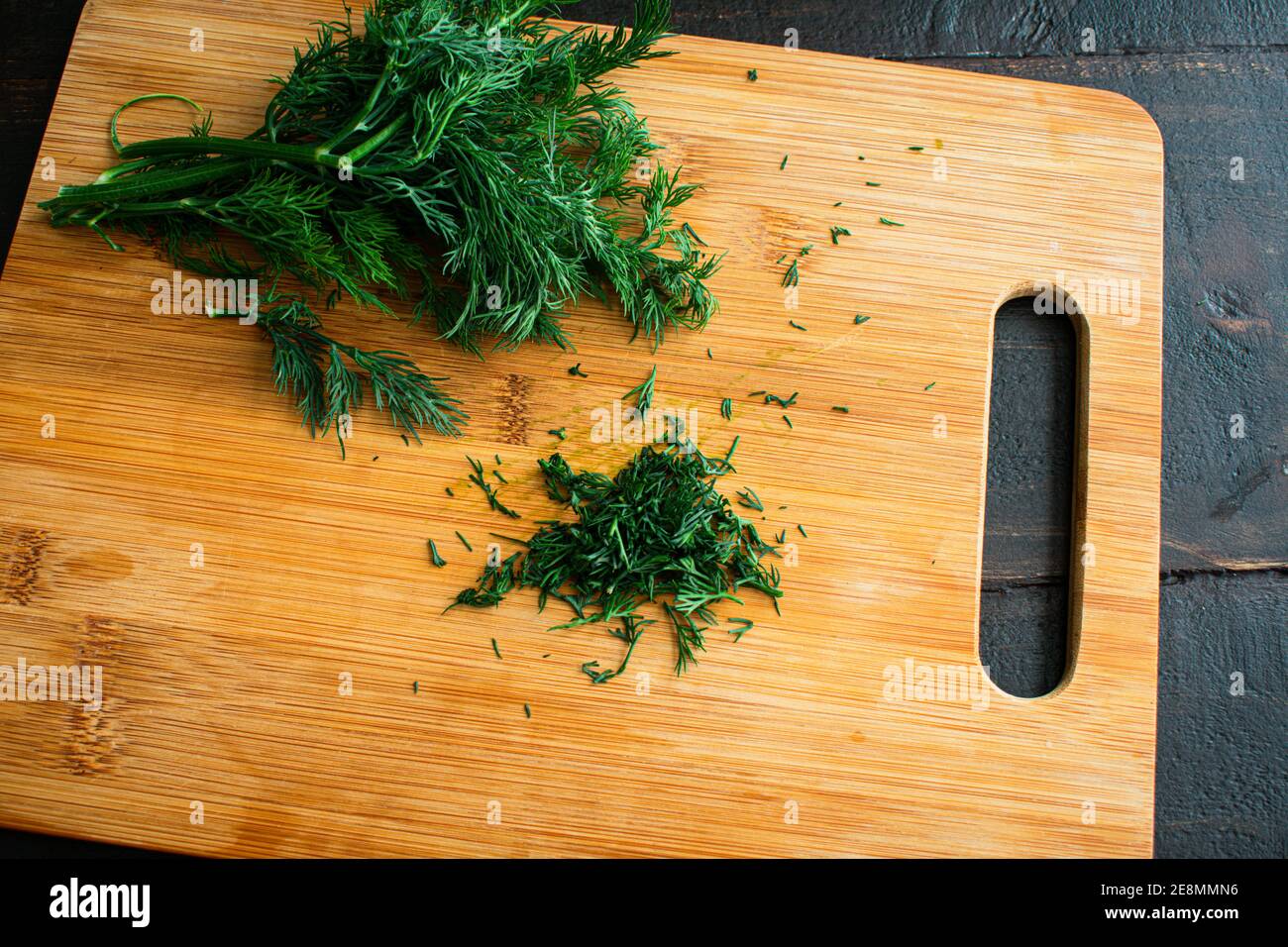 Aneto tritato su un tagliere di bambù: Aneto fresco tritato su un tagliere di legno Foto Stock