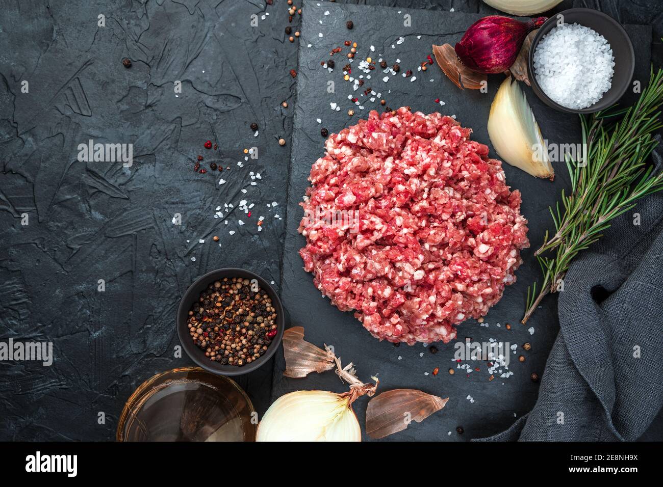 Carne fresca tritata con cipolla e rosmarino su fondo nero. Foto Stock