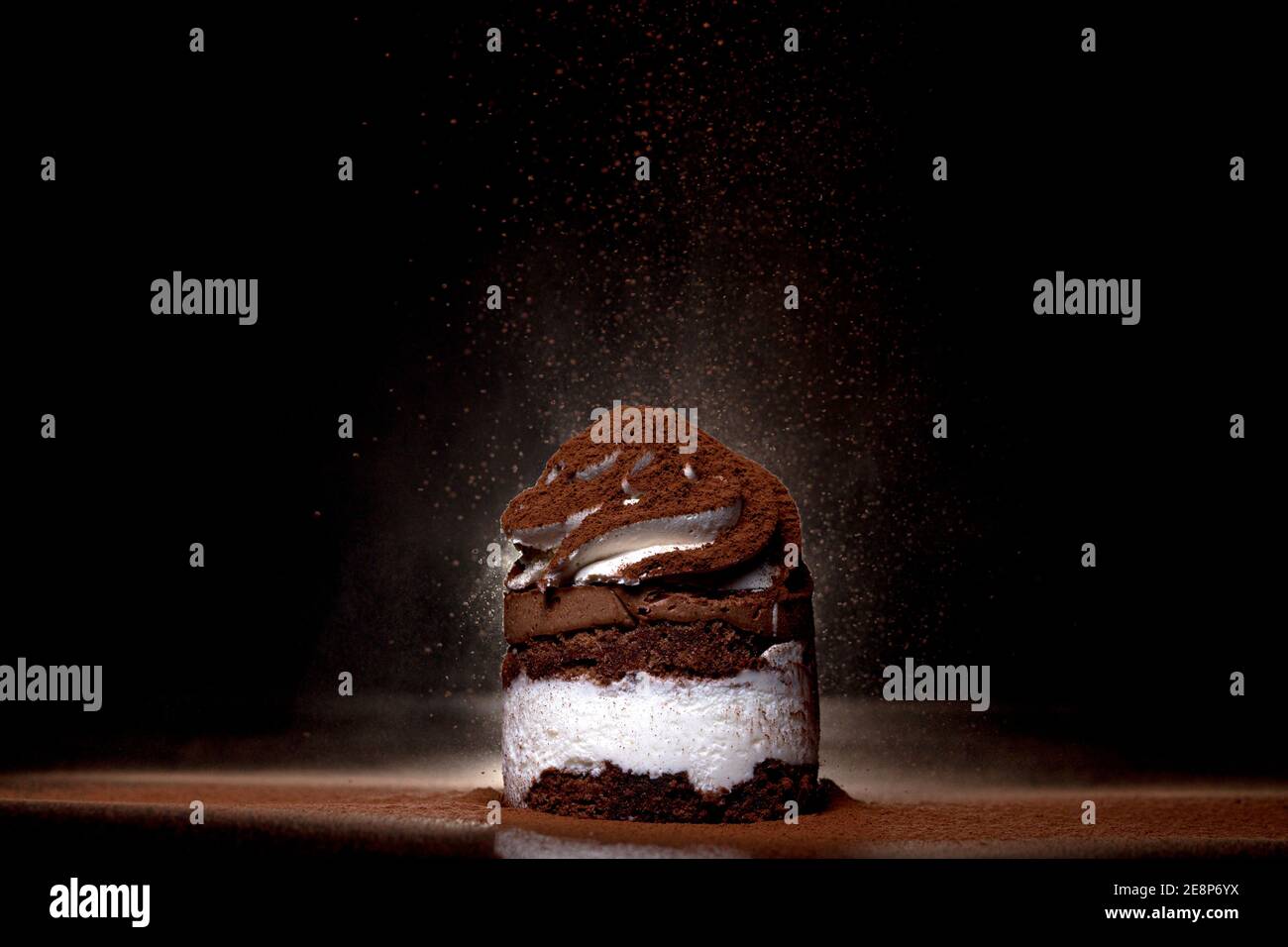 Vista laterale di una torta al cioccolato appena sfornata cosparsa di cacao sul piano di lavoro con sfondo scuro. Tasto basso. Concetto di cibo e bevande invernali. Selettivo Foto Stock