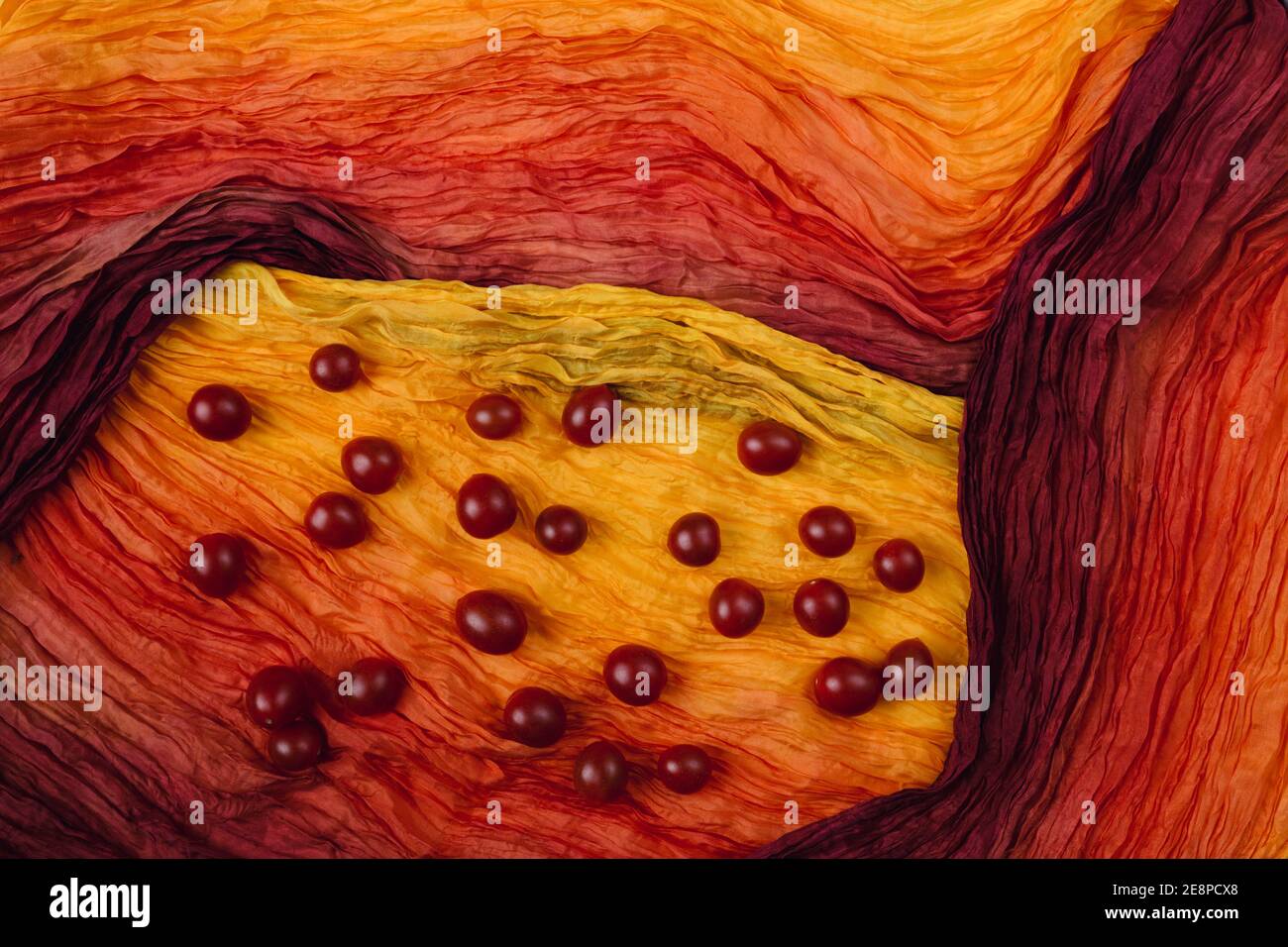 Pomodori ciliegini su fondo di tessuto di seta ondulato. Atmosfera calda ed estiva dal concetto minimo. Idea di pittura Foto Stock