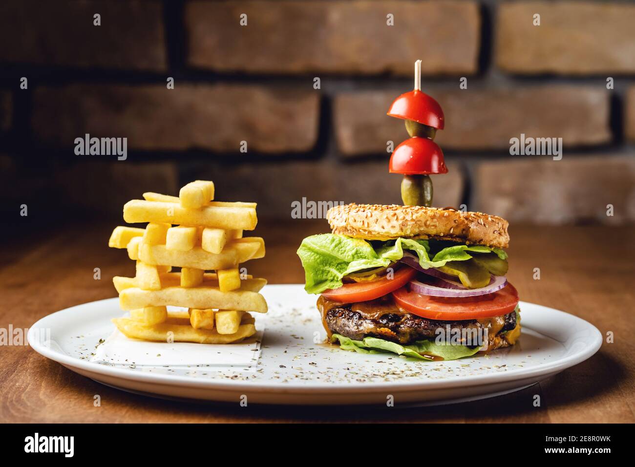 Burger con cipolla di pomodoro di manzo e foglie di lattuga su un piatto con patatine servite al ristorante Foto Stock