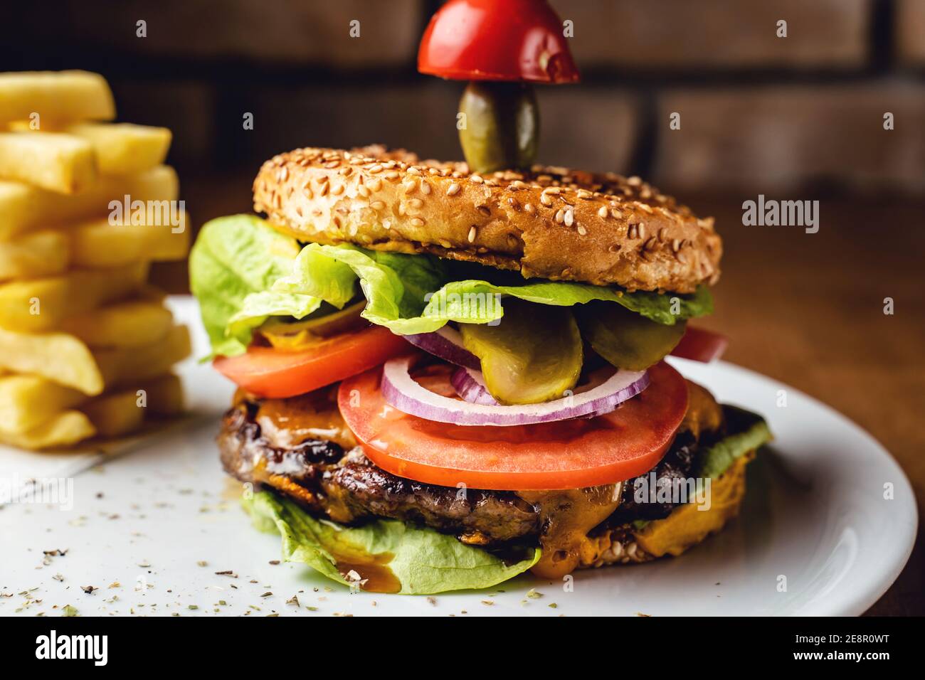 Burger con cipolla di pomodoro di manzo e foglie di lattuga su un Piatto con fondo muratura in mattoni - Burger con patatine fritte servita al ristorante Foto Stock