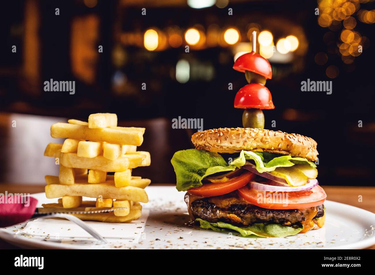 Burger con cipolla di pomodoro di manzo e foglie di lattuga su un piatto con patatine servite al ristorante Foto Stock
