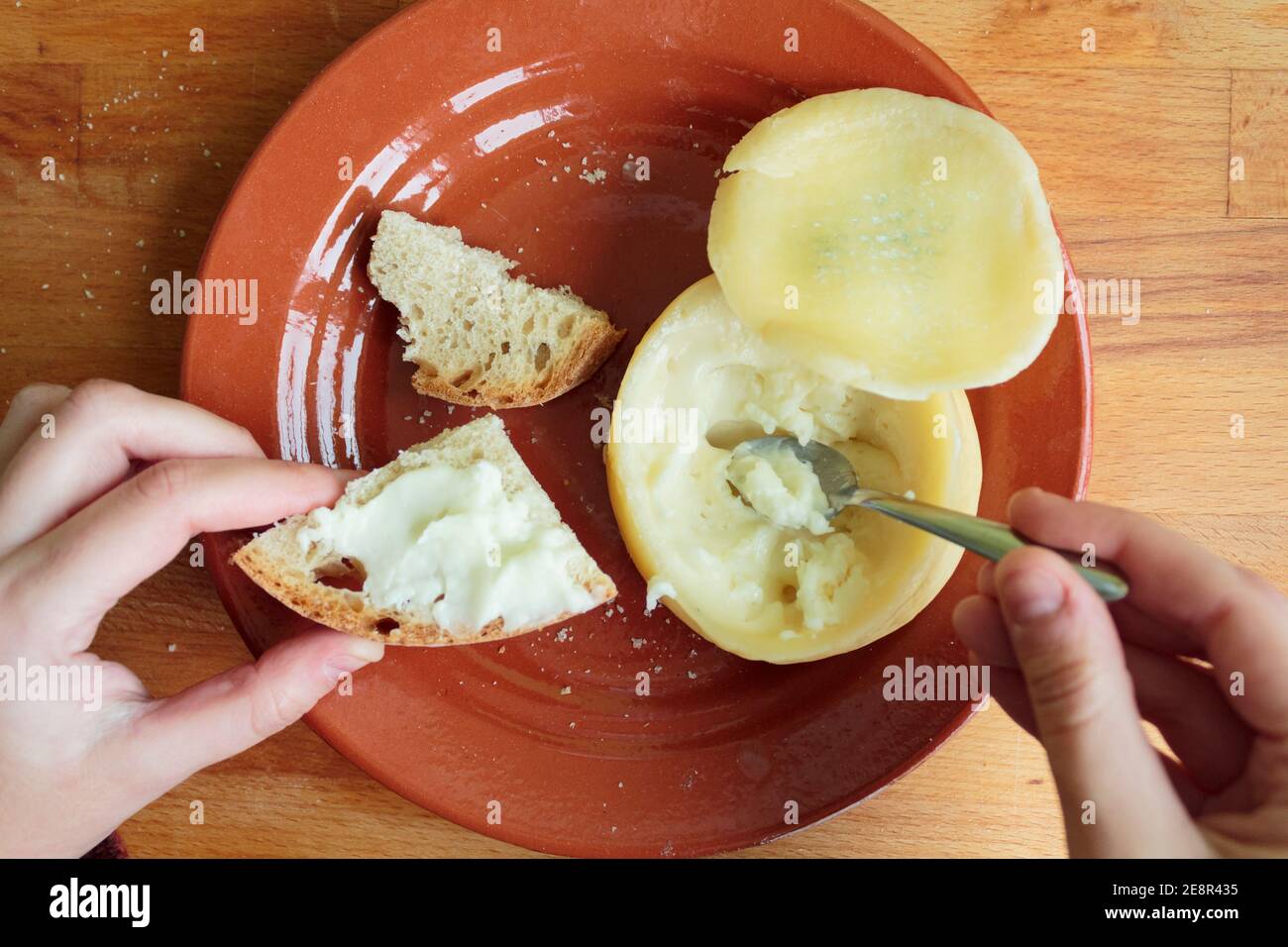 Le mani della donna che sputano formaggio morbido e cremoso su un pezzo di pane. Punto di vista personale Foto Stock