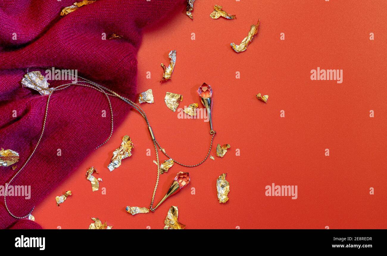 Collana e dolce cashmere rosso su sfondo rosso con luccichio. Disposizione piatta con spazio vuoto. Foto Stock