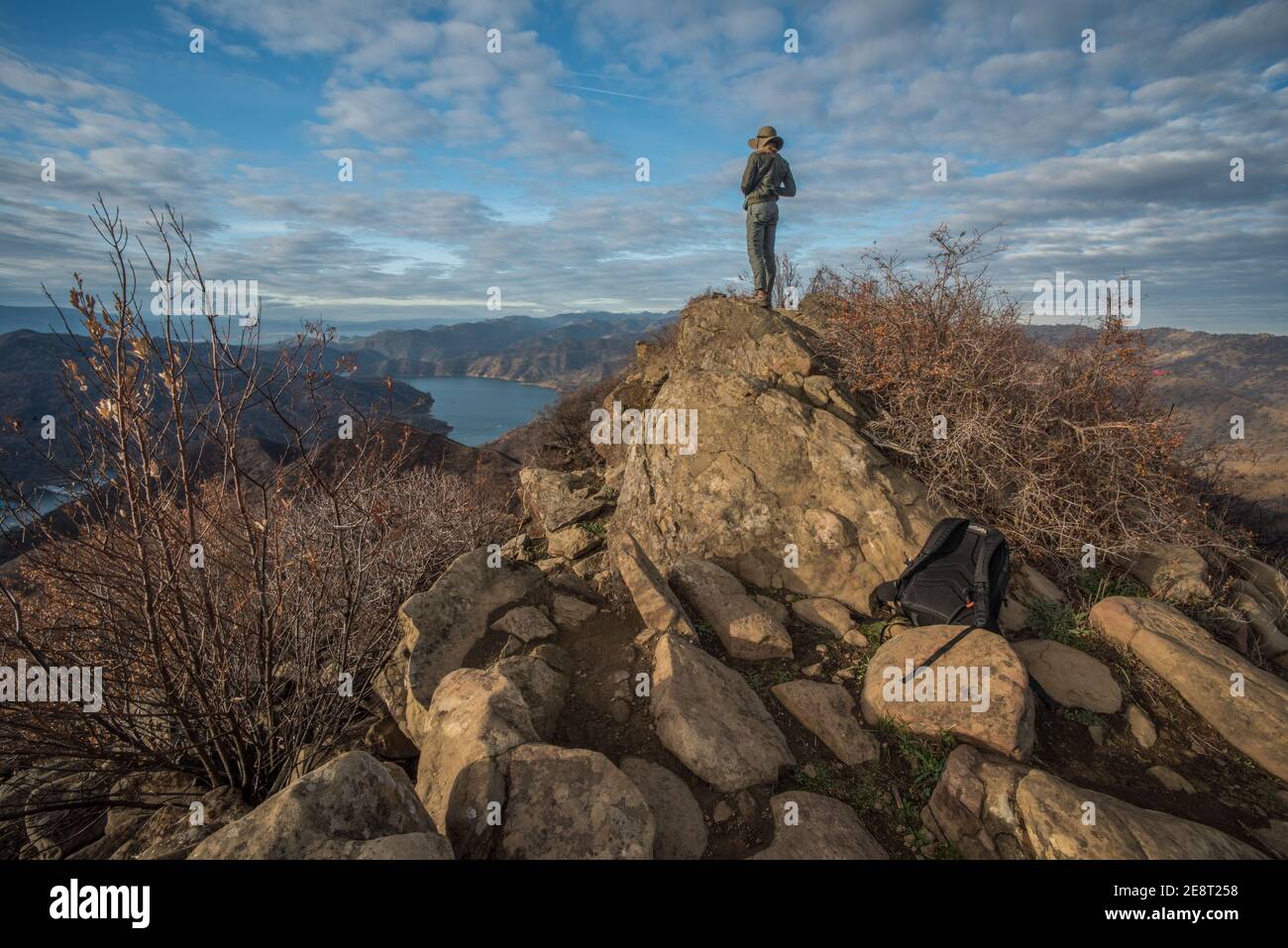 Un escursionista femminile si ferma in cima ad alcune rocce per ammirare una valle e un lago sotto nella natura selvaggia della California. Foto Stock