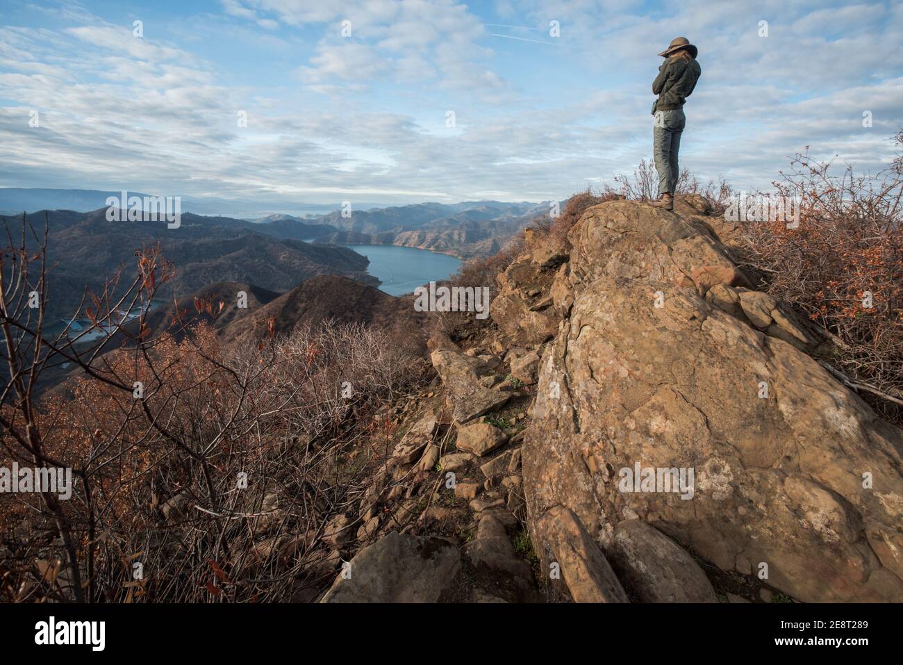 Un escursionista femminile si ferma in cima ad alcune rocce per ammirare una valle e un lago sotto nella natura selvaggia della California. Foto Stock