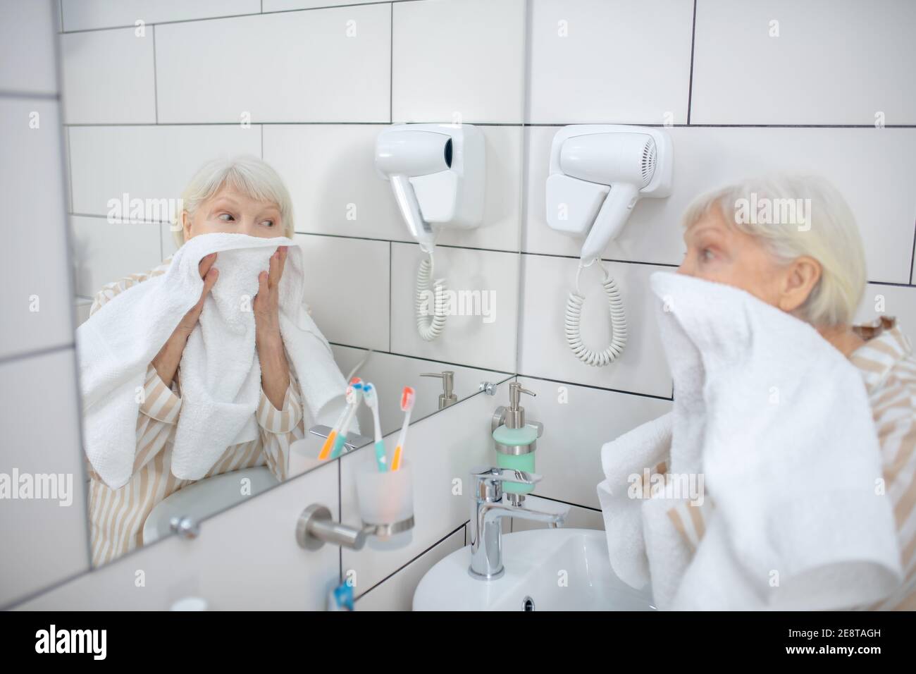 Donna dai capelli grigi che asciuga il viso con l'asciugamano Foto Stock