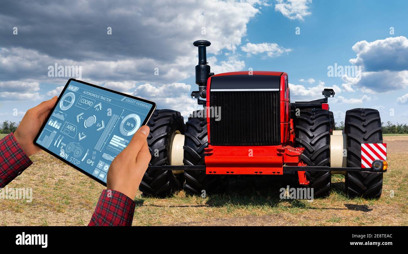 Un agricoltore con tavoletta digitale controlla un autonomo del trattore su una smart farm Foto Stock
