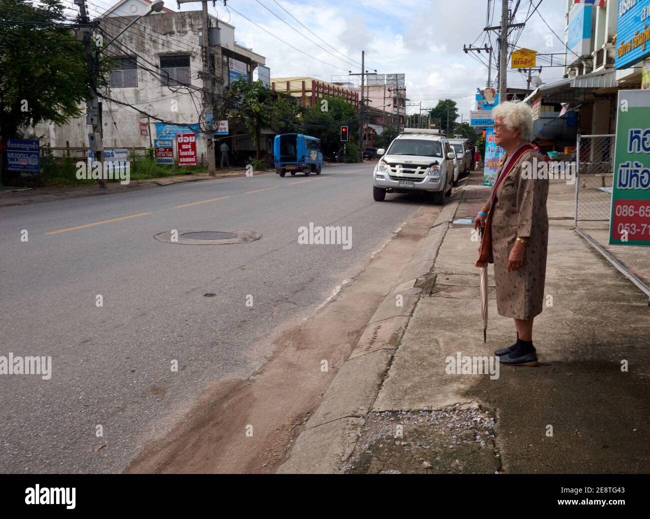 Una donna anziana si trovava sul lato della strada in attesa del passaggio dei mezzi pubblici Foto Stock