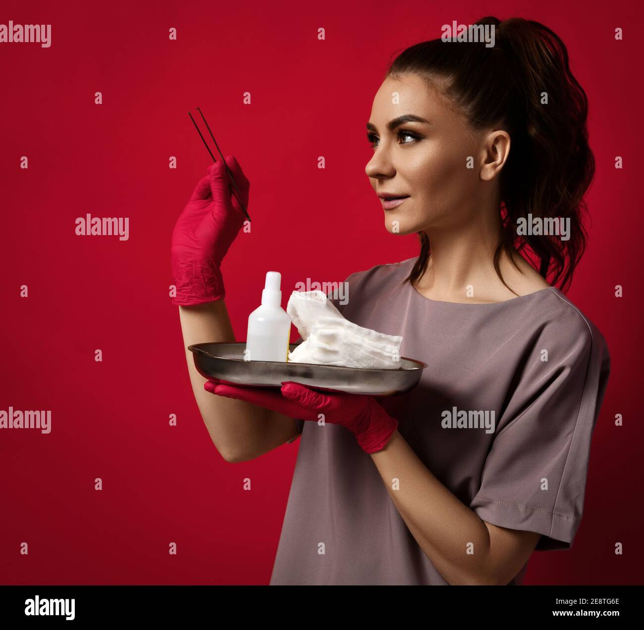 Giovane bella donna medico ginecologa in lattice guanti stand e. tenendo le pinzette in mano e gli attrezzi medici sul vassoio Foto Stock