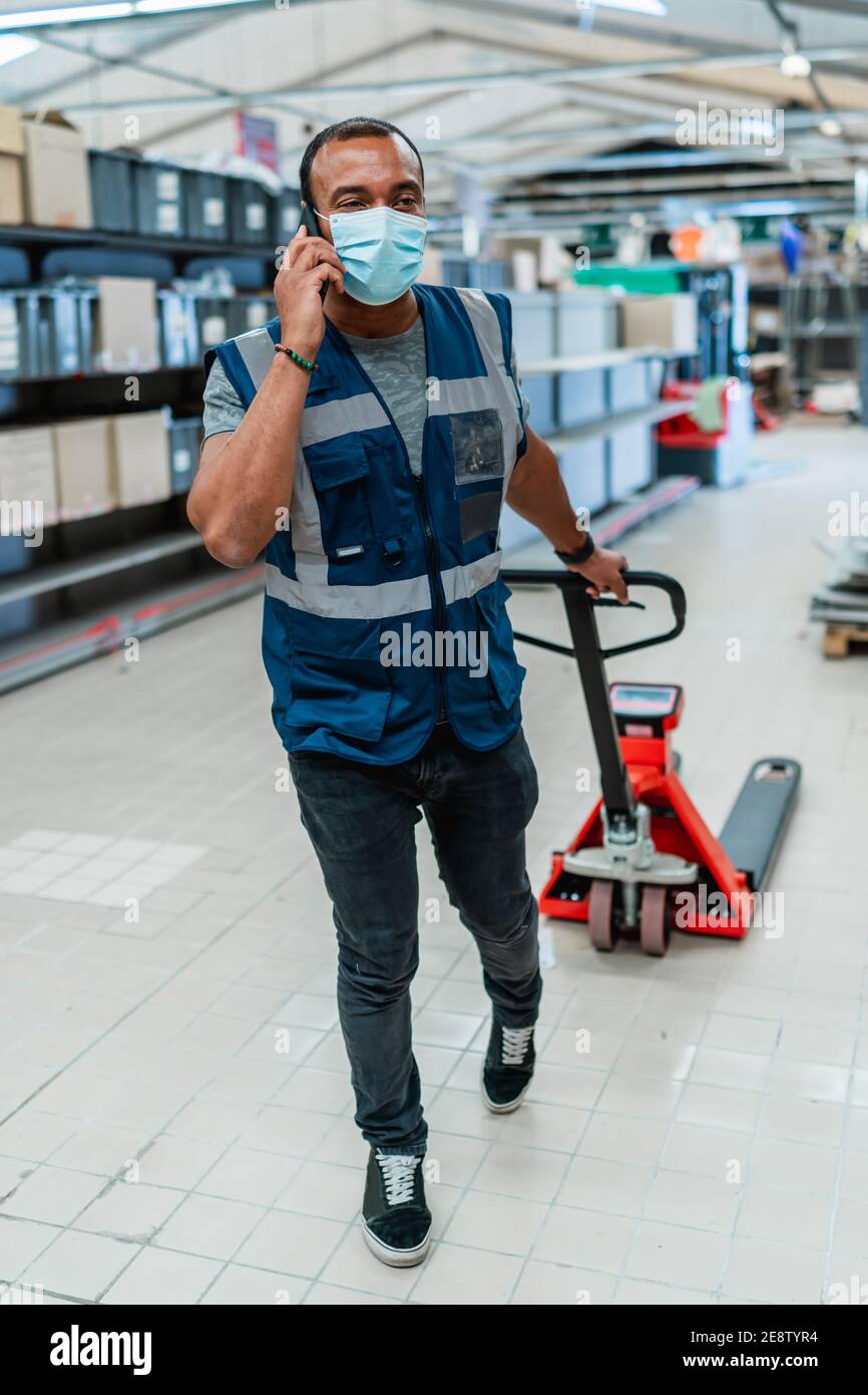 Lavoratore di magazzino di media età che tira un carrello e parla su telefono Foto Stock