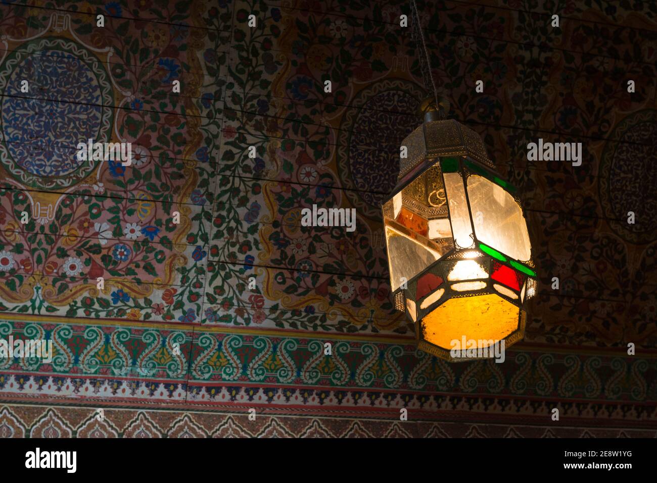 Lampada pendente appesa al soffitto in legno dipinto in una delle camere intorno al cortile del Palazzo Bahia a Marrakech, Marocco. Foto Stock
