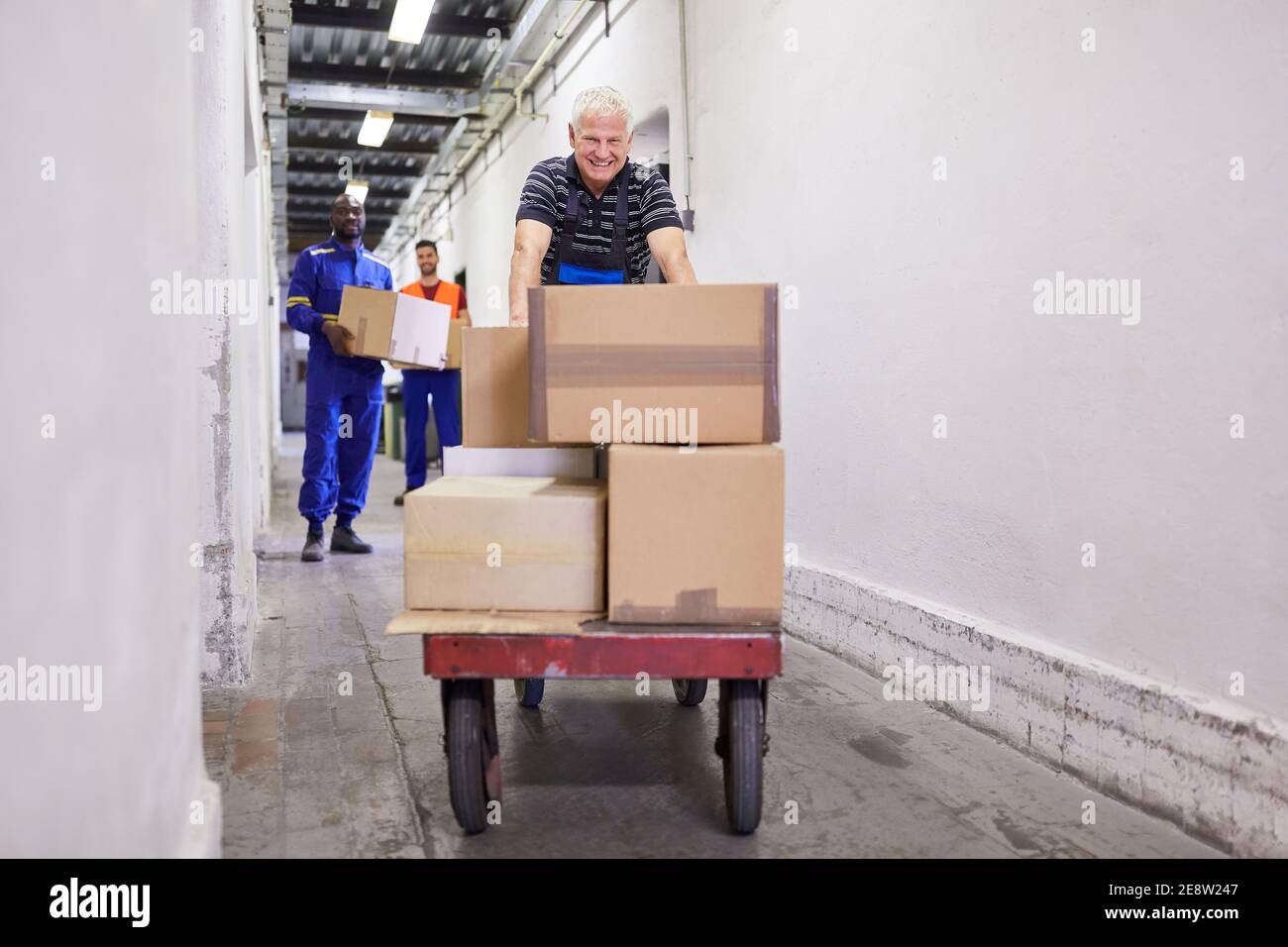 Il lavoratore trasporta i pacchi sui carrelli di spinta al magazzino di una società di spedizione o una fabbrica Foto Stock