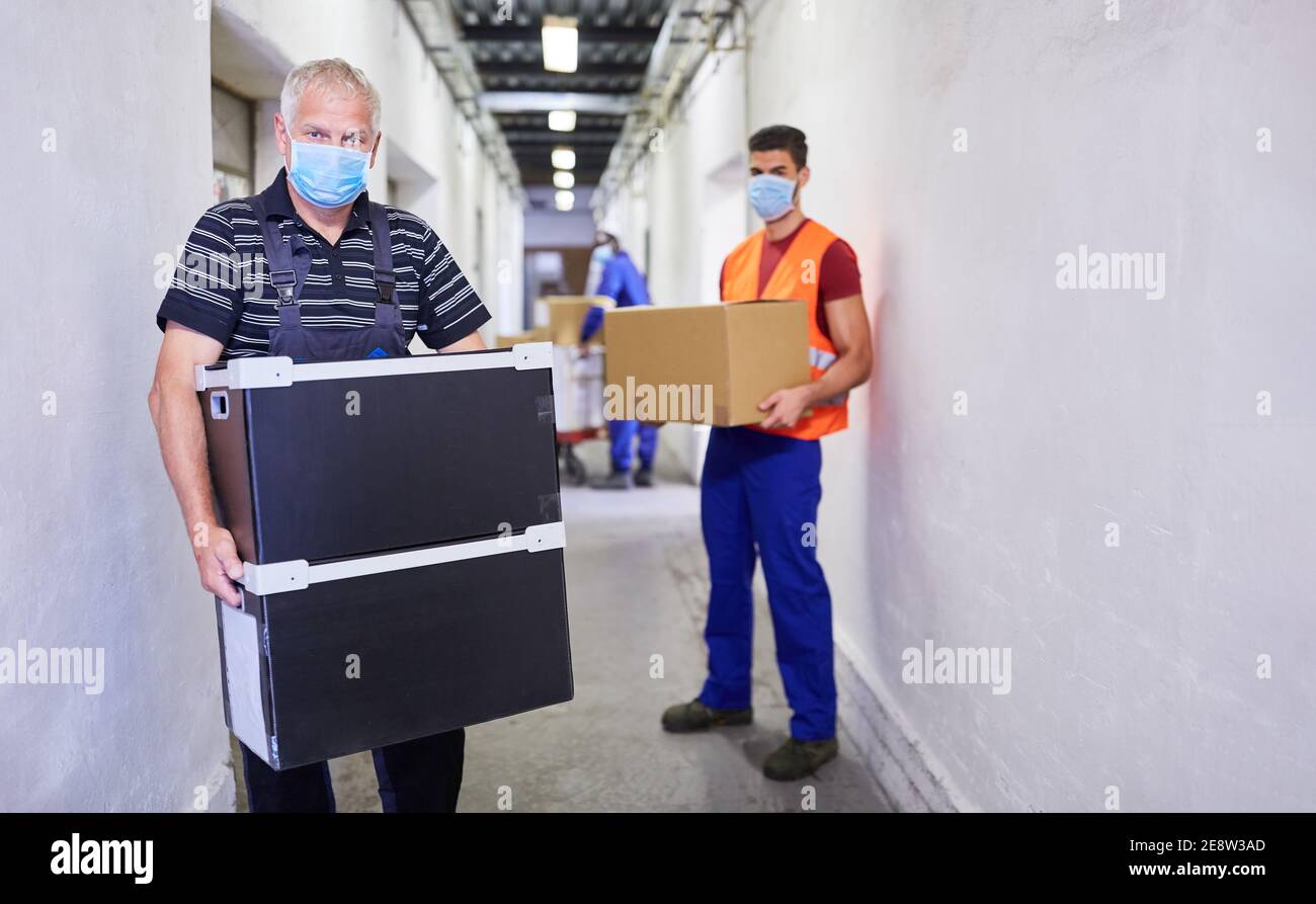 Due lavoratori con maschere a causa di Covid-19 trasportano i pacchetti in il magazzino di una fabbrica Foto Stock