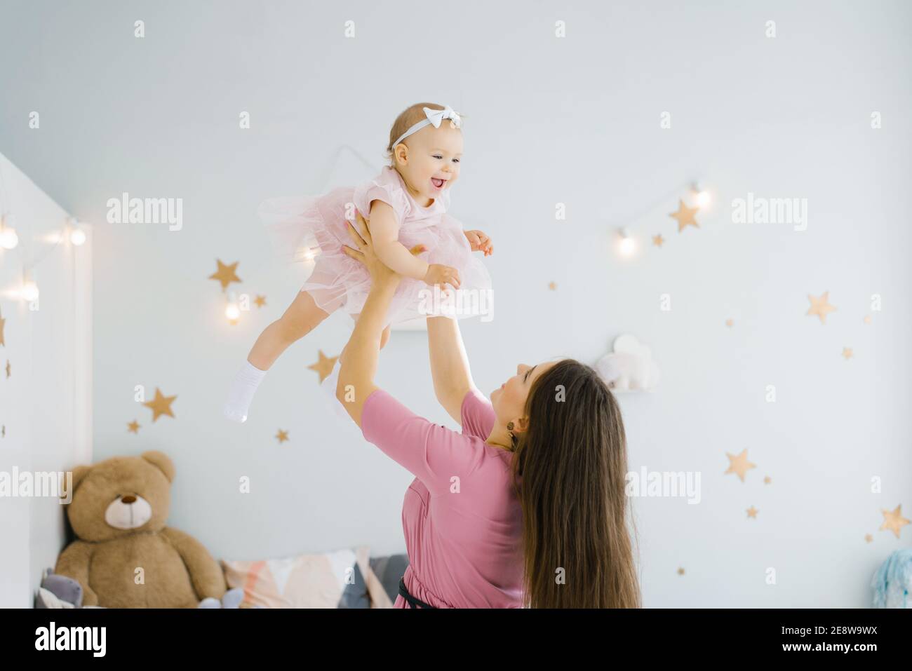 Una madre e un bambino giocano nella stanza dei bambini. Rapporti di famiglia felici. Mamma lancia una felice figlia di un anno. Foto Stock