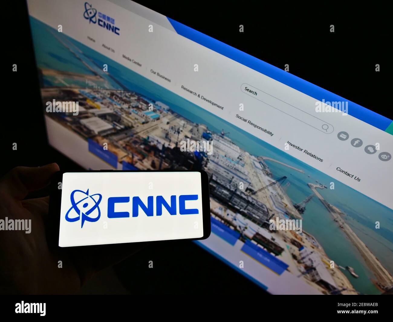 Vista ad alto angolo della persona che tiene uno smartphone con il logo della China National Nuclear Corporation (CNNC) in esposizione con il sito Web. Mettere a fuoco lo schermo del telefono. Foto Stock