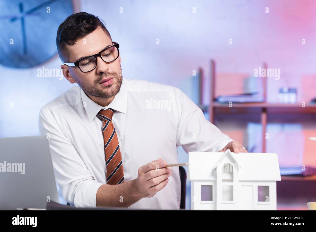 architetto serio in occhiali puntando con matita a casa maquette Foto Stock