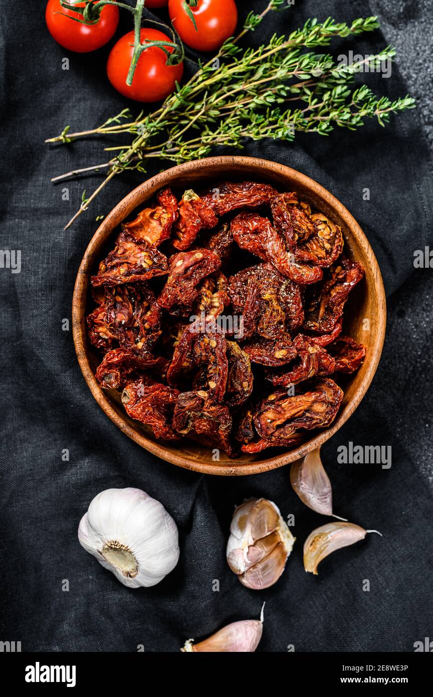 Pomodori secchi con aglio, spezie ed erbe. Ricetta per cucinare con gli ingredienti. Nero, sfondo scuro. Vista dall'alto Foto Stock
