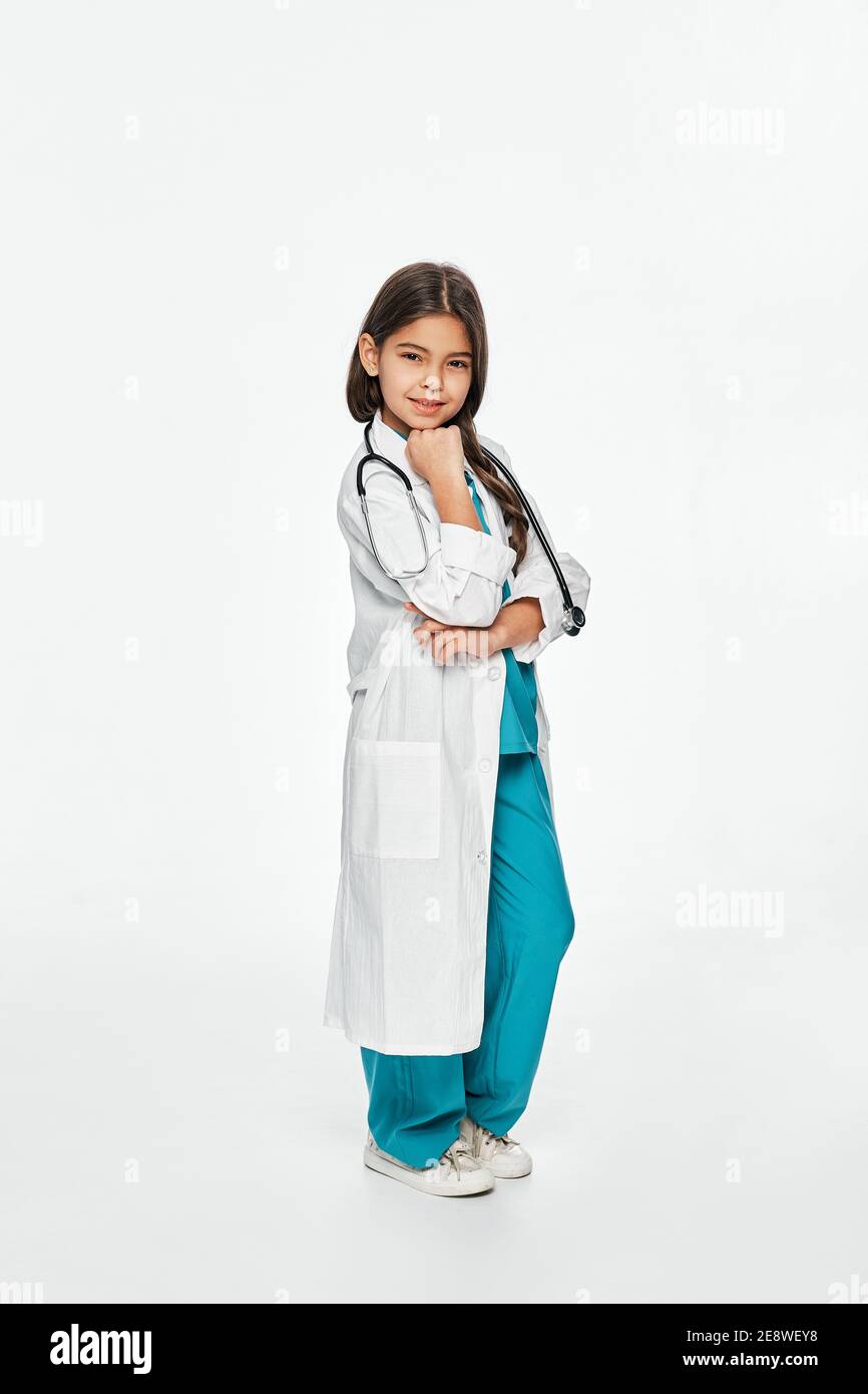 Bambina latina che indossa un cappotto medico e stetoscopio, posa e guardando la macchina fotografica. Isolato su bianco Foto Stock