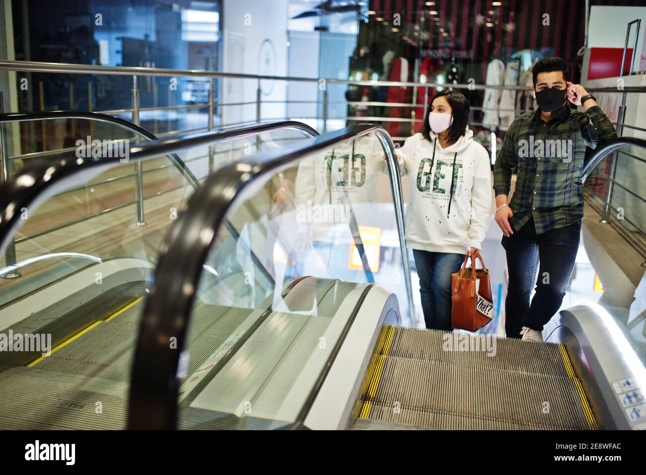 Le coppie asiatiche indossano maschere facciali arrampicano la scala mobile presso il centro commerciale. Foto Stock