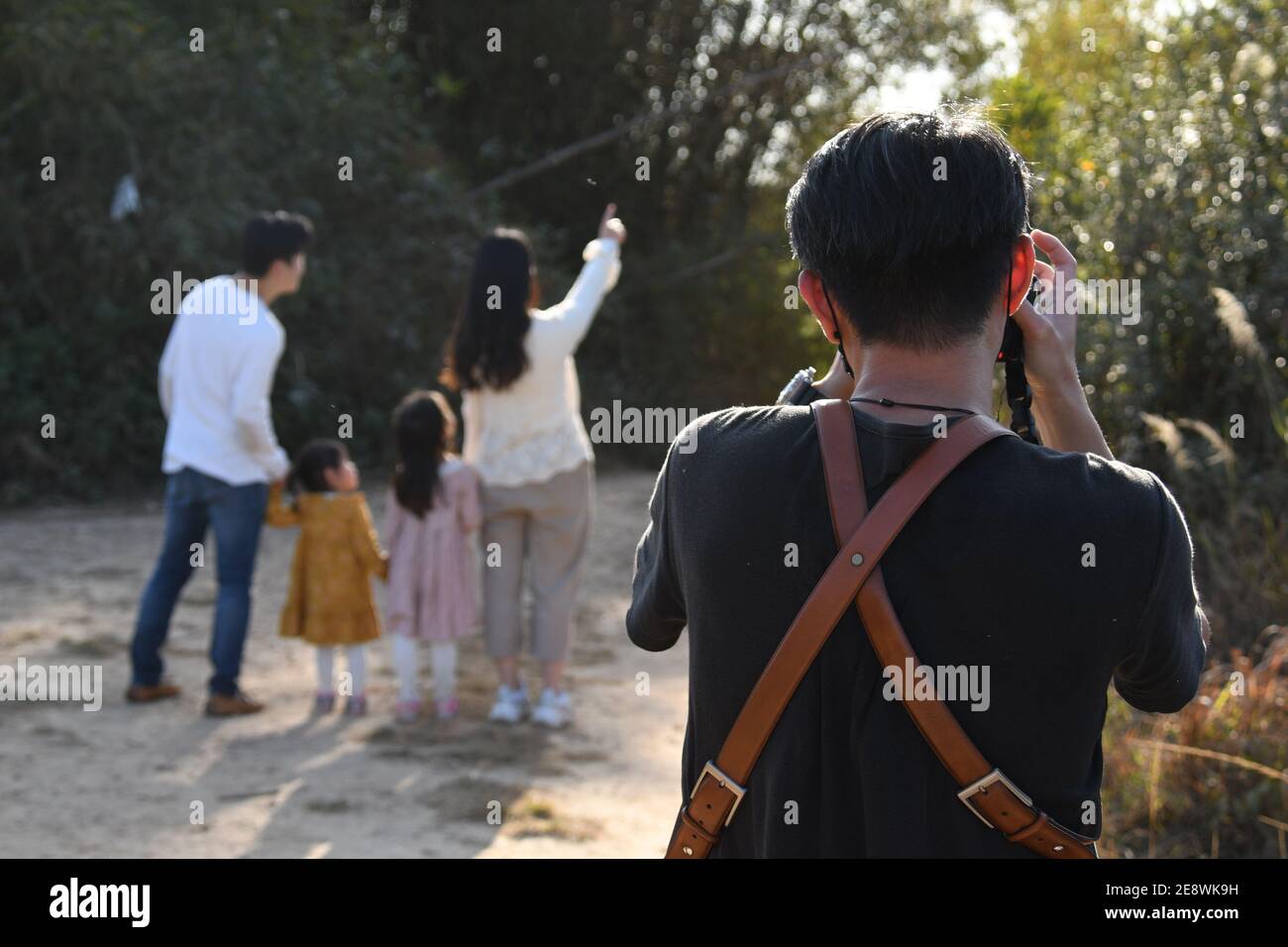 Vista posteriore di un fotografo asiatico che fotografa una famiglia in un campo nella zona di Fanling, Hong Kong Foto Stock