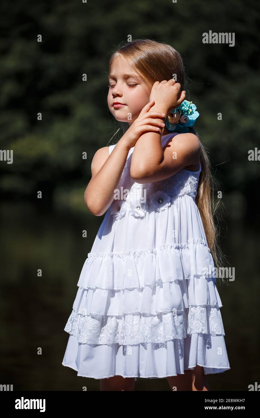 Una bambina carina di 6 o 7 anni con lunghi capelli biondi, è vestita in un  abito estivo balletto, è in piedi sullo sfondo del fiume Foto stock - Alamy