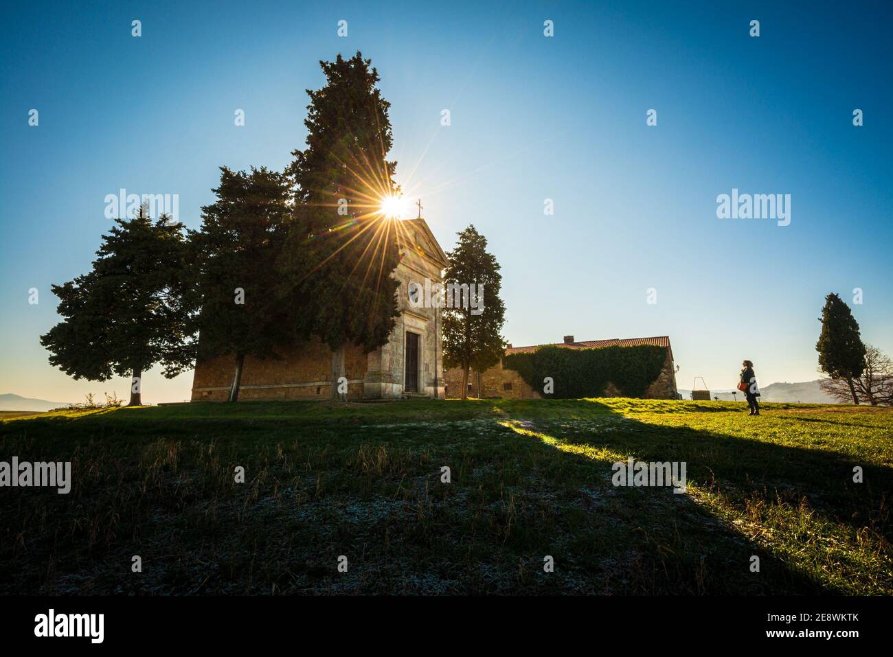 Una chiesa di Vitaleta retroilluminato con il sole che si apre appena dietro un cipresso Foto Stock