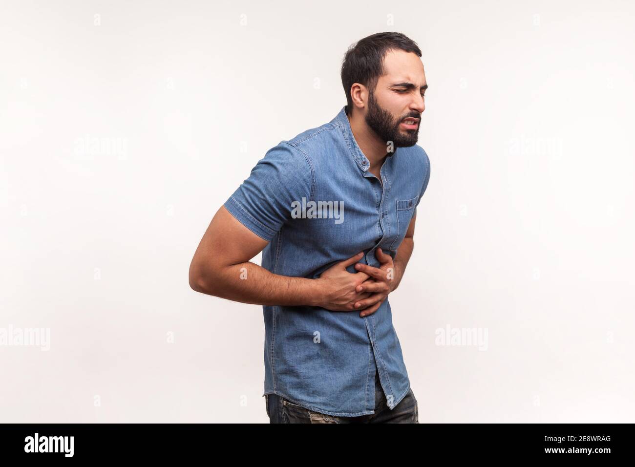 Malcontento uomo depresso con barba che tiene le mani sullo stomaco sensazione di dolore acuto, indigestione e nausea, ulcera duodenale. Studio interno girato iso Foto Stock