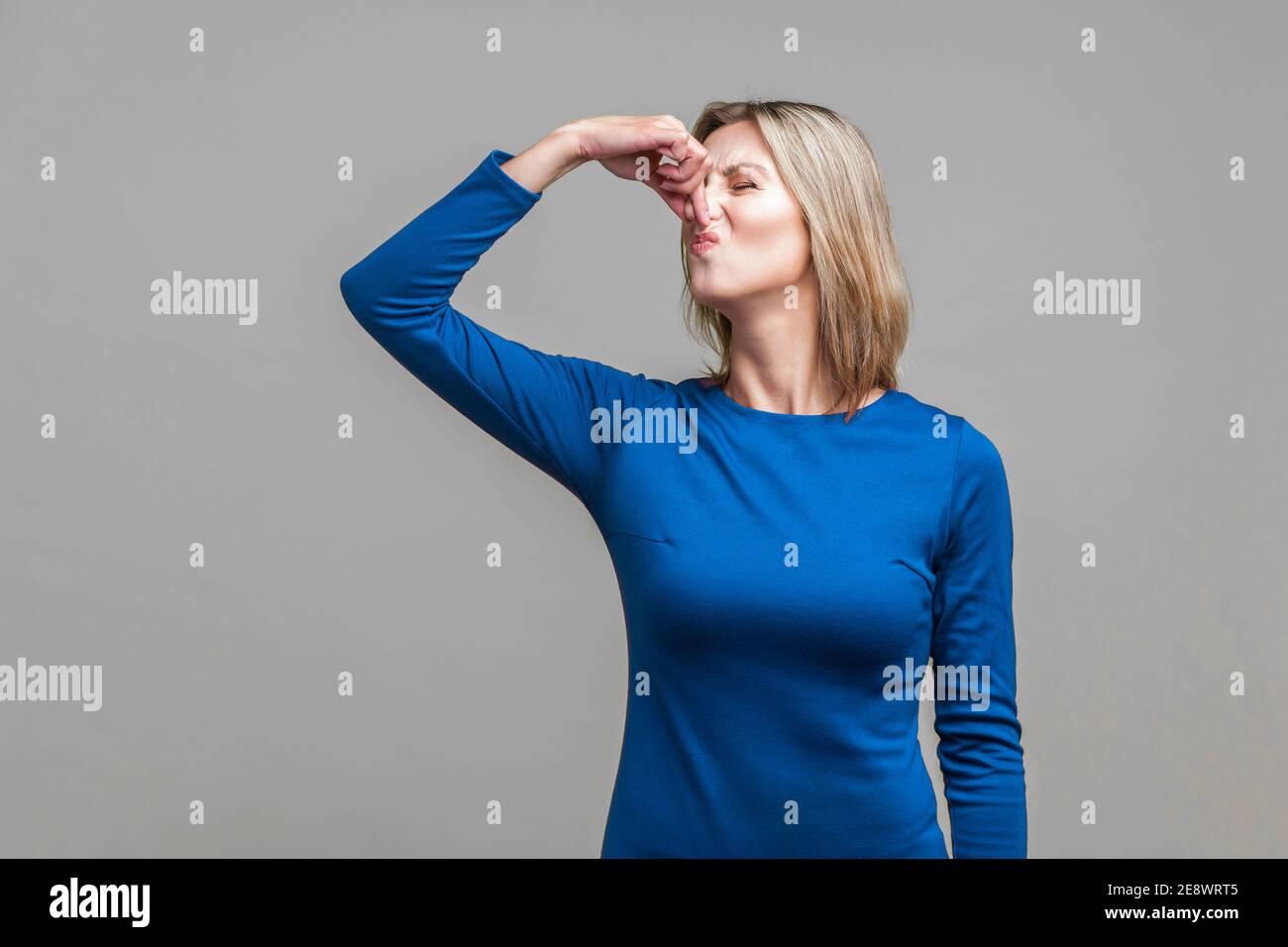 Cattivo odore. Ritratto di giovane donna in abito blu che sta stringendo il naso con le dita per trattenere il respiro, disgustato da puzza insopportabile. Indoor Foto Stock
