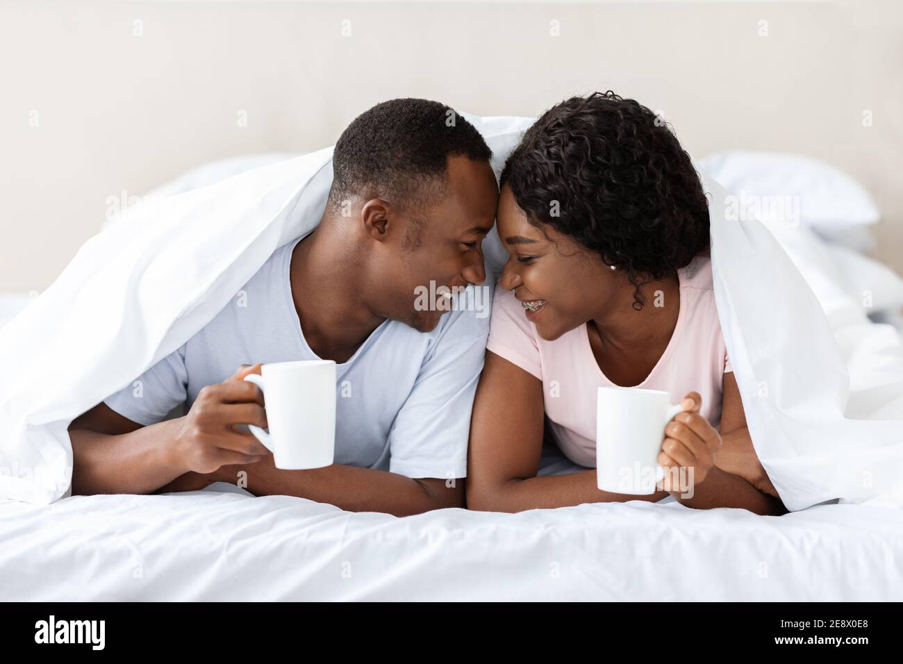 Romantica coppia nera che si posa sotto la coperta, bere tè Foto Stock