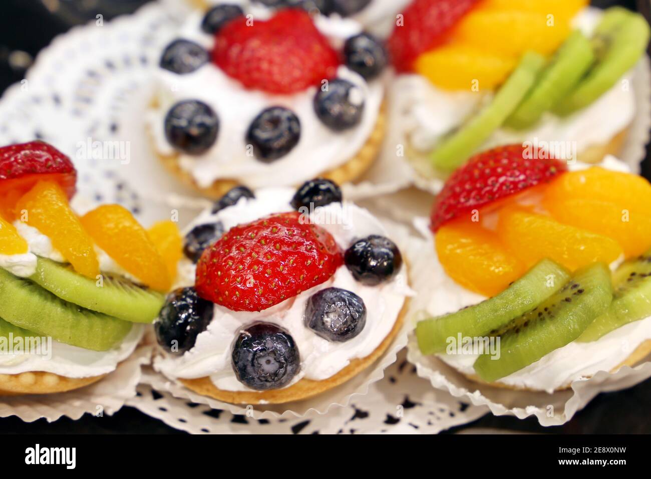 Torte cremose con frutta fresca e frutti di bosco. Dolce con mandarino, kiwi, fragola e mirtilli Foto Stock