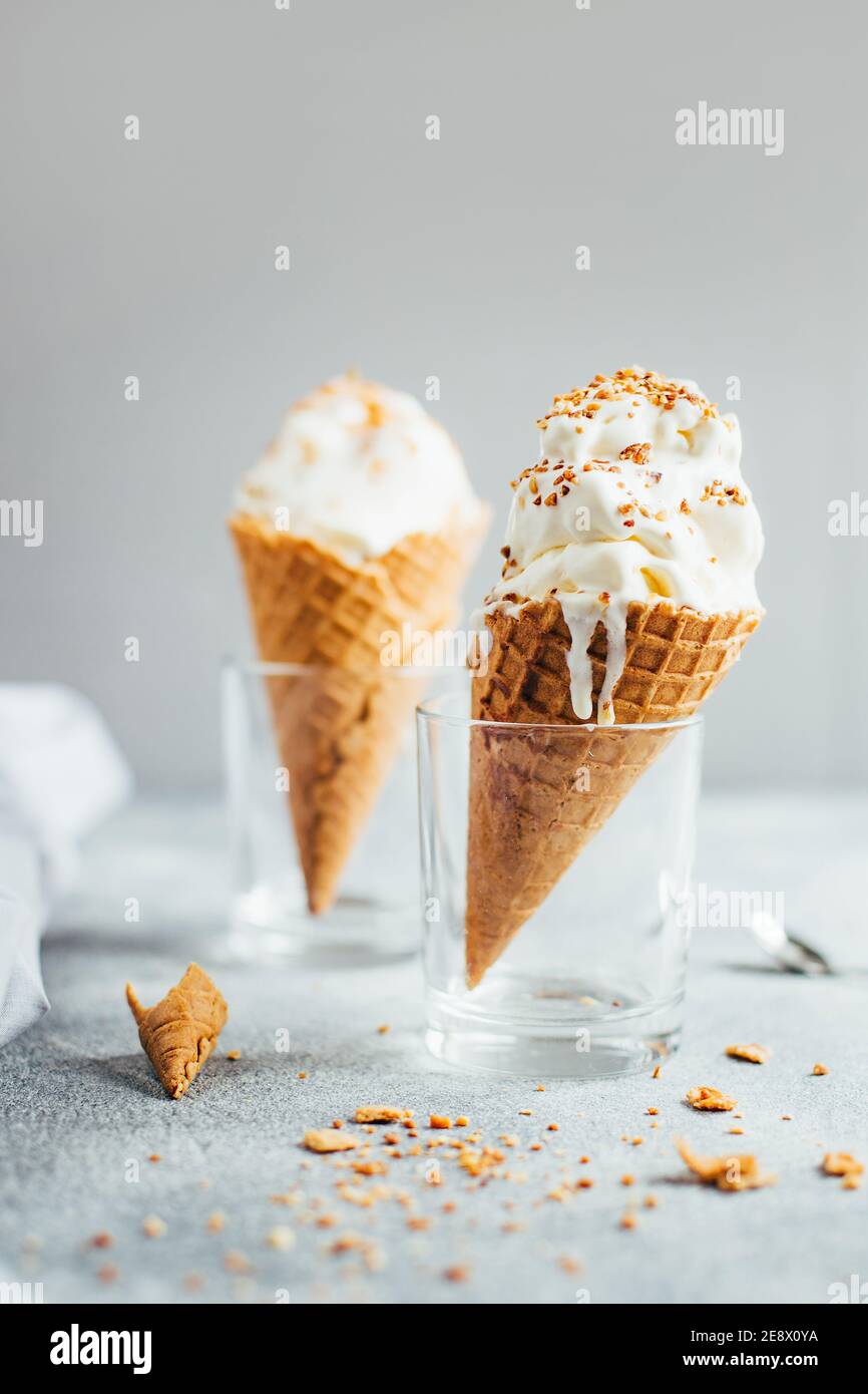 primo piano su gelato alla vaniglia bianca in una tazza di waffle in un vetro trasparente su un tavolo grigio e grigio sfondo Foto Stock