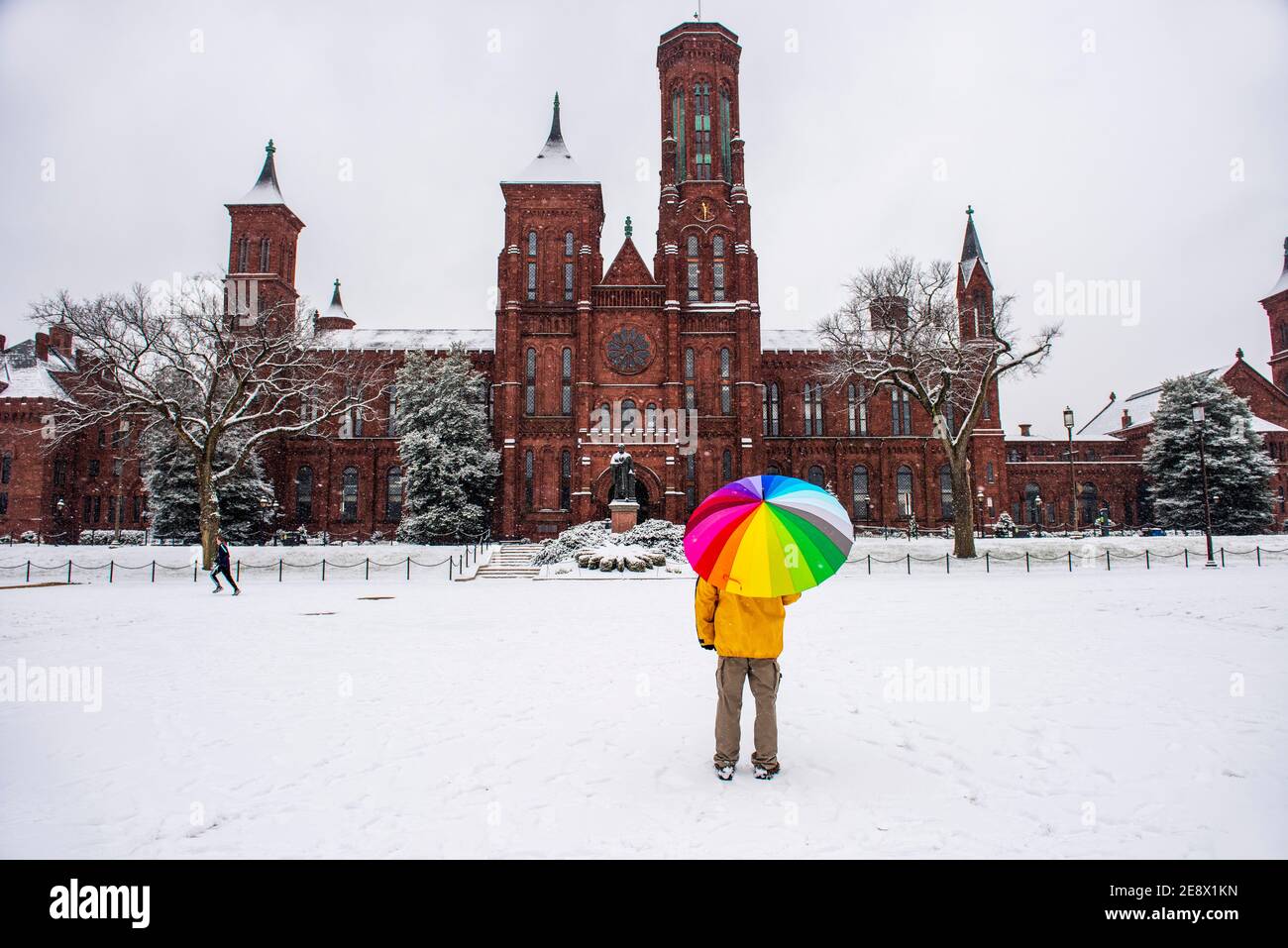 Un uomo con un ombrello colorato si ferma di fronte allo Smithsonian Institution Building, conosciuto anche come il Castello, durante una giornata innevata a Washington, D.C. Foto Stock