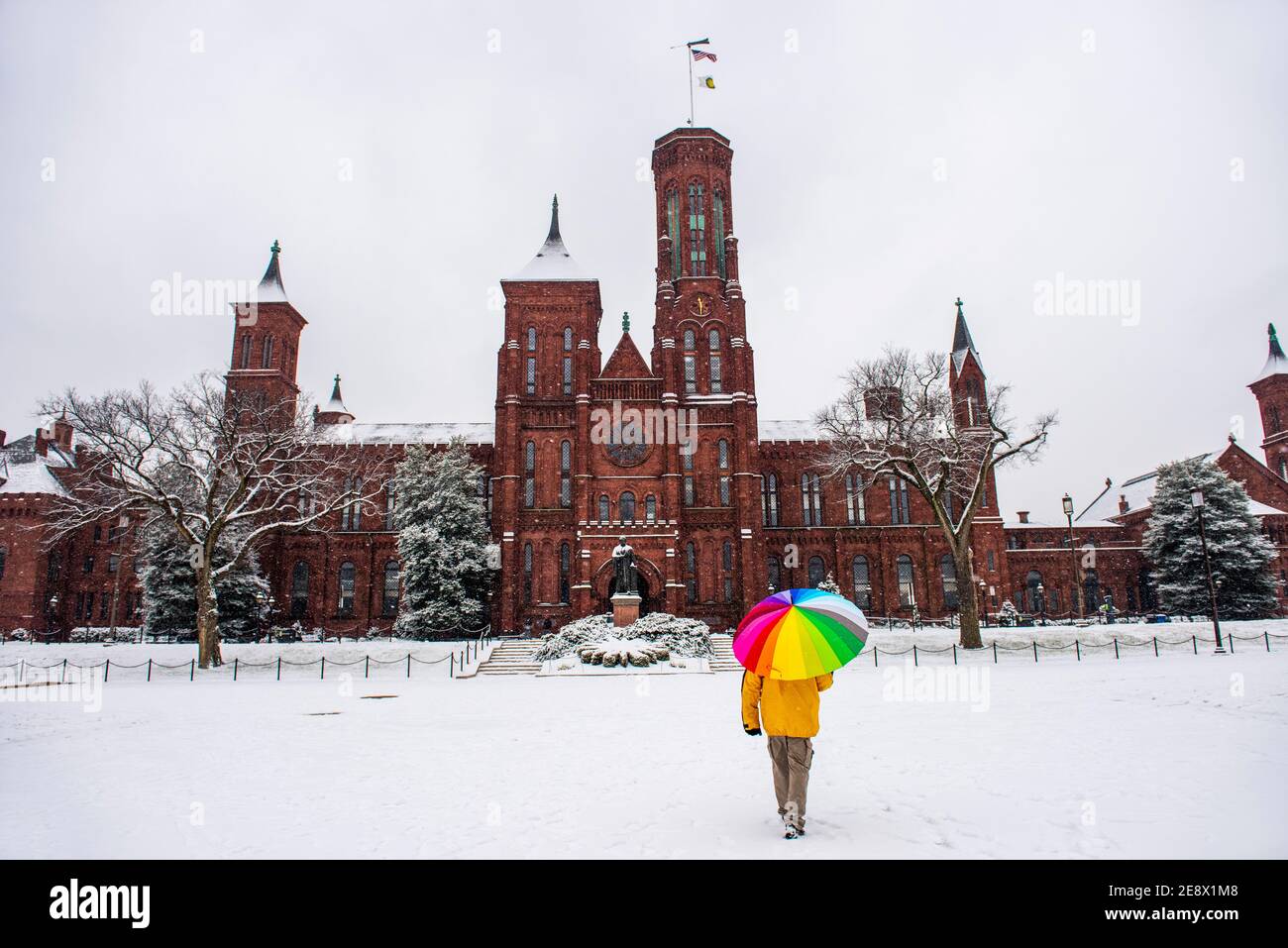 Un uomo con un ombrello colorato si ferma di fronte allo Smithsonian Institution Building, conosciuto anche come il Castello, durante una giornata innevata a Washington, D.C. Foto Stock