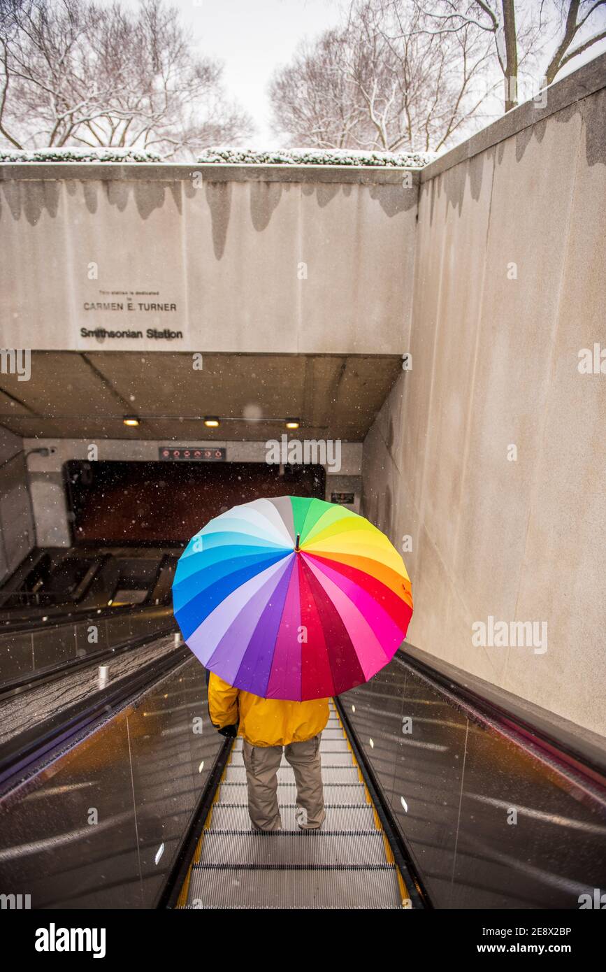 Un uomo che porta un ombrello di colore arcobaleno guida la scala mobile Metro a Washington, D.C. Foto Stock
