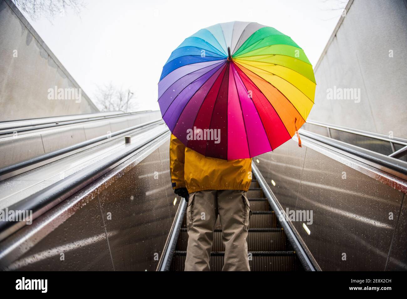 Un uomo che porta un ombrello di colore arcobaleno guida la scala mobile Metro a Washington, D.C. Foto Stock